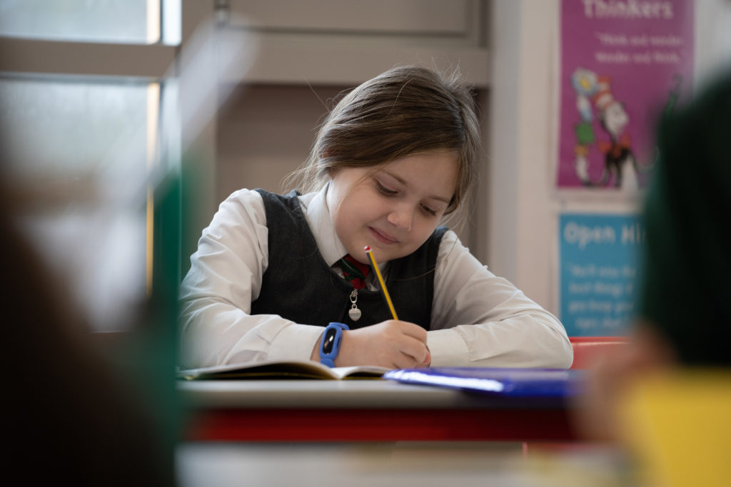 A young girl is seen working hard on a piece of work with a pencil in her right hand.
